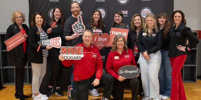 A group posing for a picture in front of an SIUE alumni association backdrop with cougar mascot