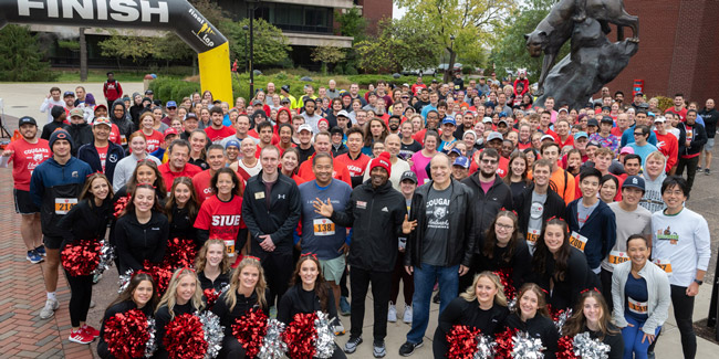 A group dancing outdoors centering on a woman mid-motion in an SIUE Cougars shirt