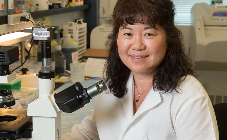 A faculty member of the SIUE School of Pharmacy sitting next to a microscope