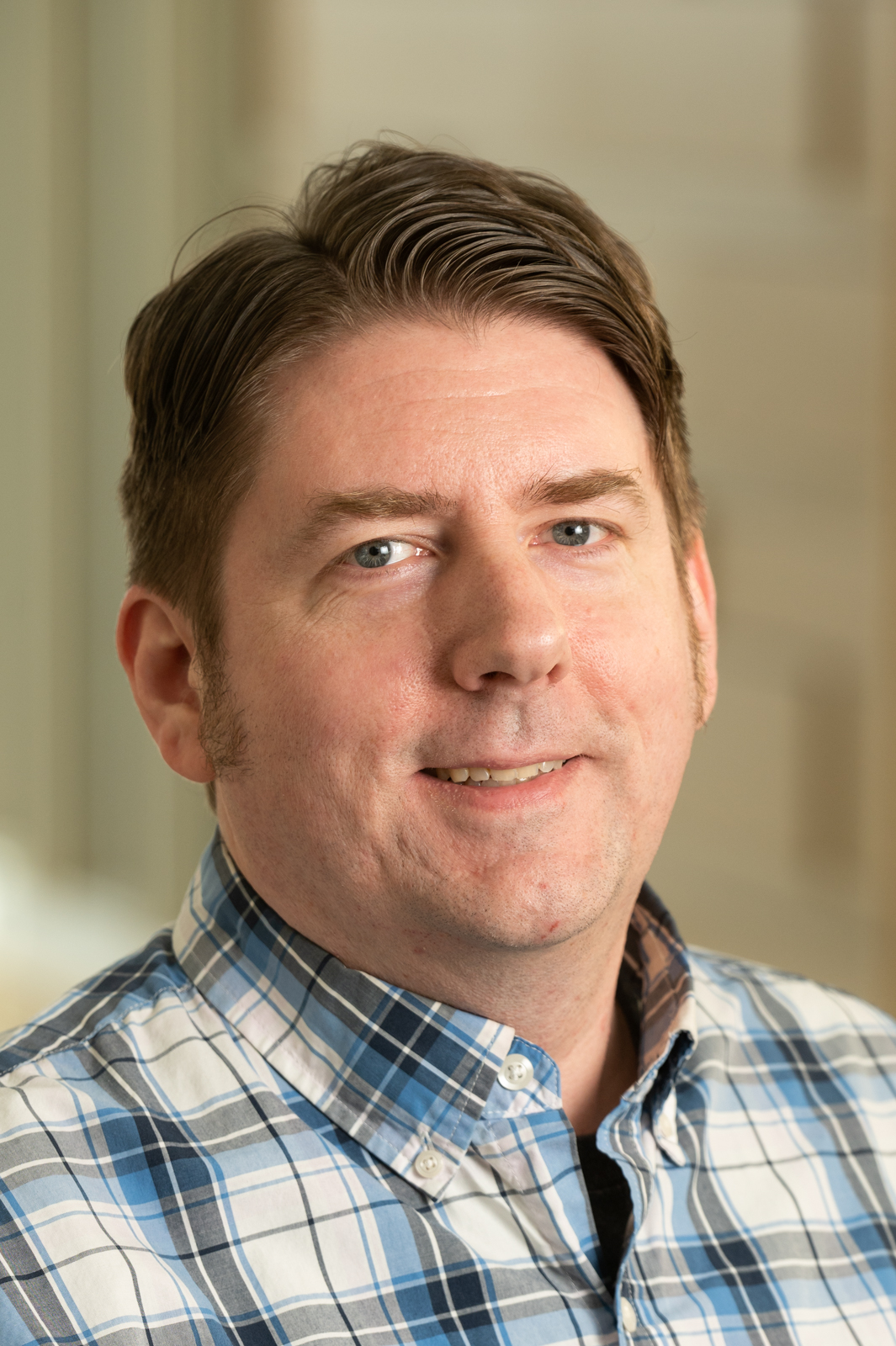 A portrait of Andy Koch, a middle-aged, fair-complected man. Andy is smiling and wearing a plaid shirt.