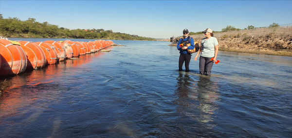 Two women standing in a river across from large orange buoys