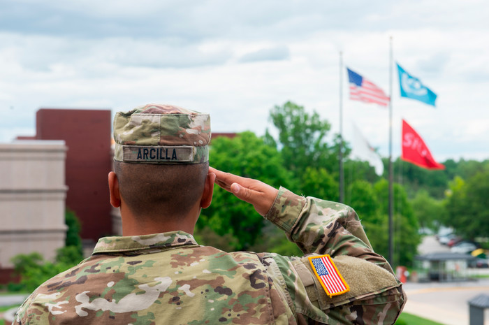 Photo of Serviceman Arcilla saluting the American flag, the SIUE flag, and the state of Illinois flag, it is a haze overcase day and the perspective is on the servicemans salute. 