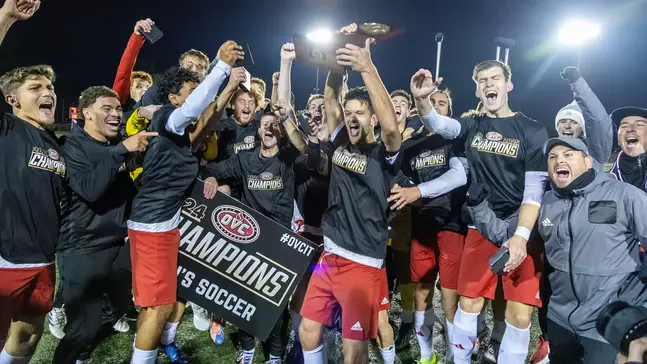 mens soccer team celebrating a win and wearing OVC champions tshirts on the pitch at night with their arms in the air and their mouths open wide